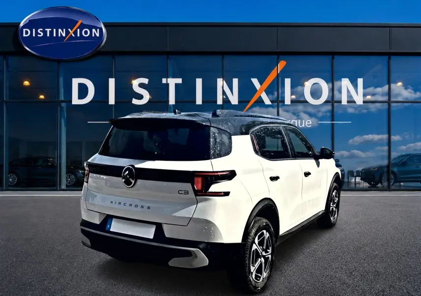 Vue 3/4 arrière droite d'un Citroën C3 Aircross blanc avec toit noir et jantes alu devant un showroom Distinxion.