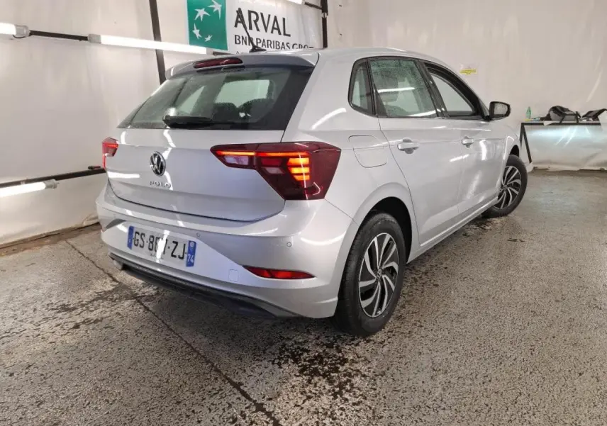 Vue 3/4 arrière droit d'une Volkswagen Polo gris clair avec feux arrière allumés dans un garage.