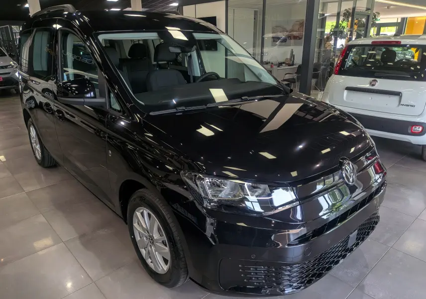 Volkswagen Caddy noir vue 3/4 avant droit en intérieur, avec phares LED et jantes alliage visibles.