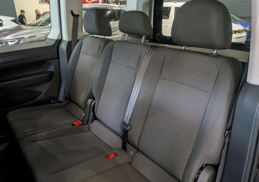 Vue intérieure des sièges arrière en tissu gris du Volkswagen Caddy 2.0 TDI noir, montrant trois appuie-têtes et ceintures de sécurité.