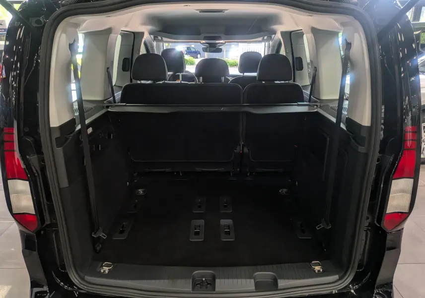 Vue arrière ouverte du Volkswagen Caddy noir 2025, montrant l'espace de chargement et les sièges arrière en tissu noir.
