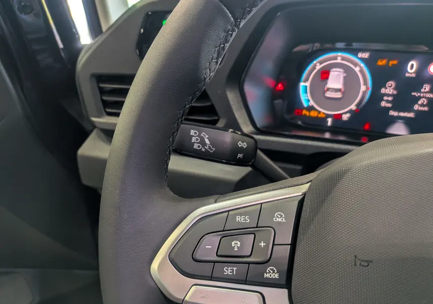 Gros plan sur le volant noir du Volkswagen Caddy 2025 avec commandes de régulateur et tableau de bord numérique.