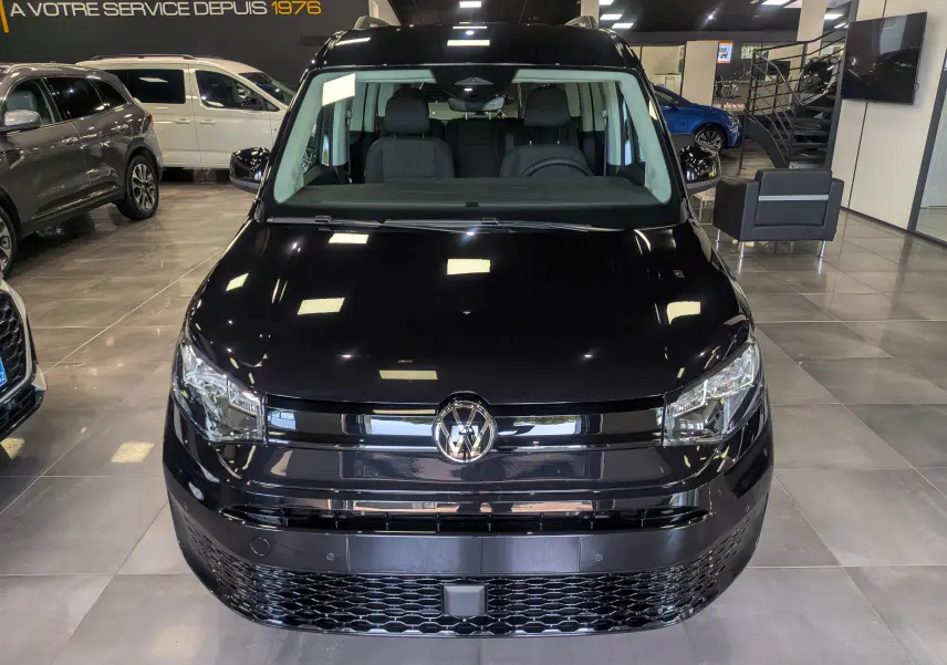 Vue avant d'un Volkswagen Caddy noir 2025 exposé en showroom, mettant en valeur sa calandre et ses phares modernes.