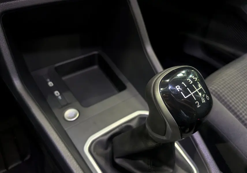 Gros plan sur le levier de vitesses manuel noir du Volkswagen Caddy 2.0 TDI 102 CH, intérieur tissu gris.