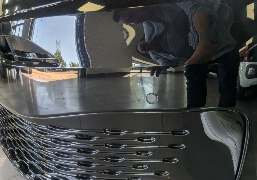 Gros plan sur la calandre noire brillante du Volkswagen Caddy 2.0 TDI 2025 avec reflet et capteur de stationnement visible.