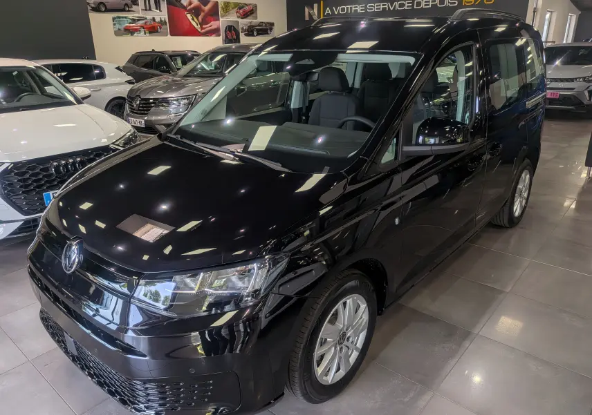 Volkswagen Caddy noir vue 3/4 avant droit en intérieur, avec jantes alliage et calandre brillante.