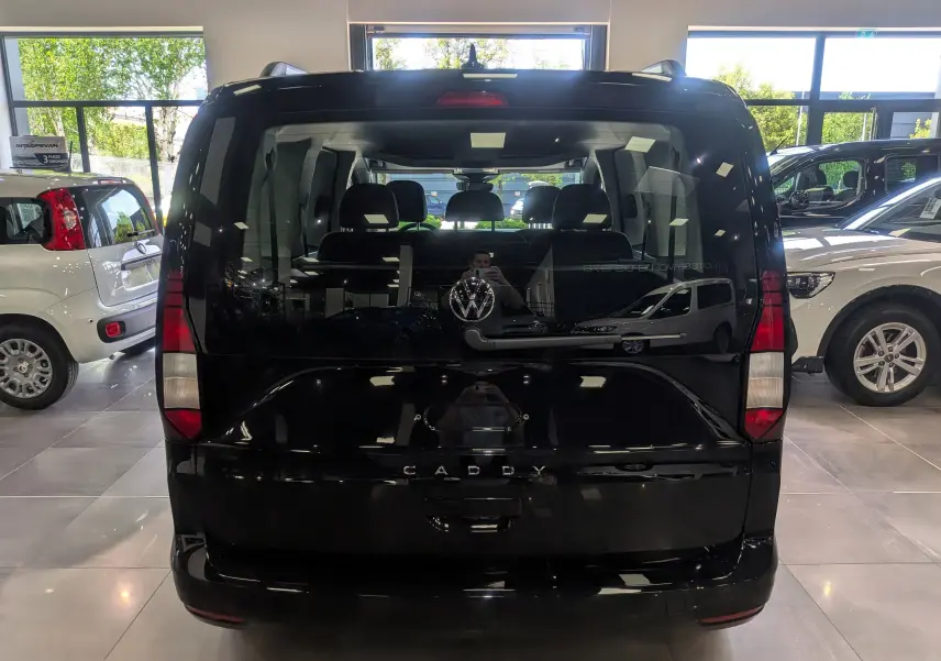 Vue arrière d'un Volkswagen Caddy noir 2025 dans un showroom, avec logo VW et vitres teintées.