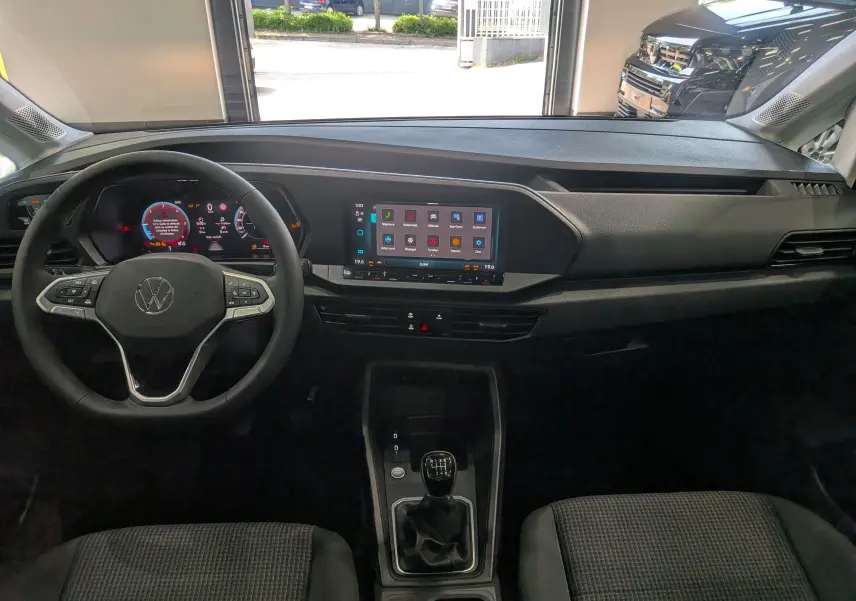 Vue intérieure frontale du tableau de bord noir du Volkswagen Caddy 2025 avec volant multifonction et écran tactile central.
