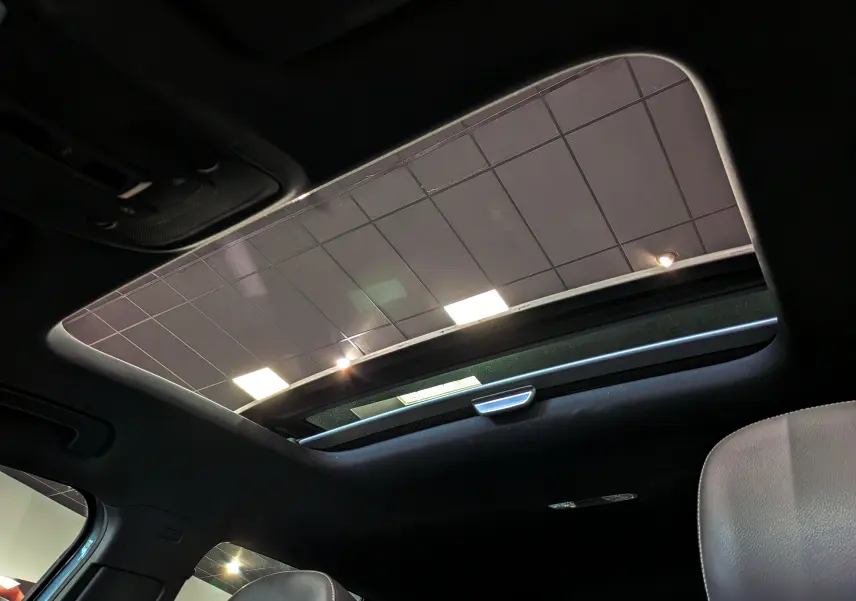 Toit ouvrant panoramique ouvert vu de l'intérieur d'un Audi Q2 gris, avec ciel de toit noir et siège cuir visible.