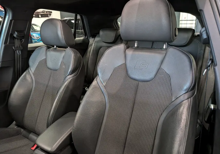 Gros plan sur les sièges avant en cuir noir avec logo S de l'Audi Q2 gris, intérieur sportif et élégant.