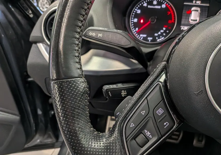 Gros plan sur le volant cuir noir et le tableau de bord avec compte-tours rouge d’un Audi Q2 gris, version 2017.