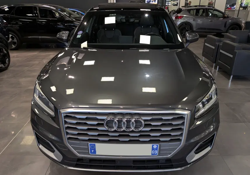 Vue frontale d'un Audi Q2 gris métallisé exposé en showroom avec calandre hexagonale et logo quatre anneaux.