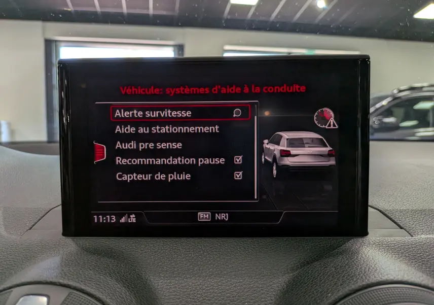 Écran central affichant les systèmes d’aide à la conduite d’un Audi Q2 gris, vue intérieure frontale.