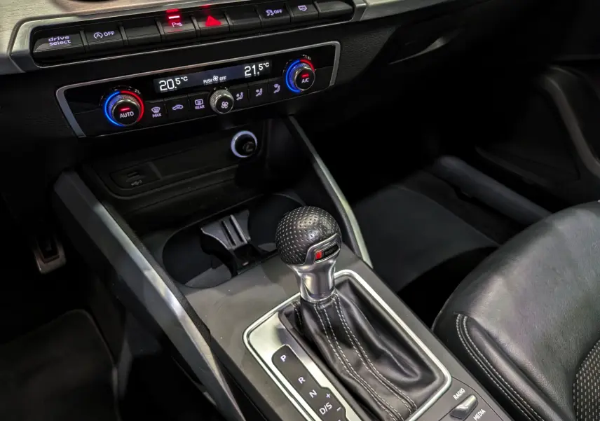 Gros plan sur la console centrale de l'Audi Q2 gris, mettant en valeur le levier de vitesse automatique S-Tronic et la climatisation digitale.