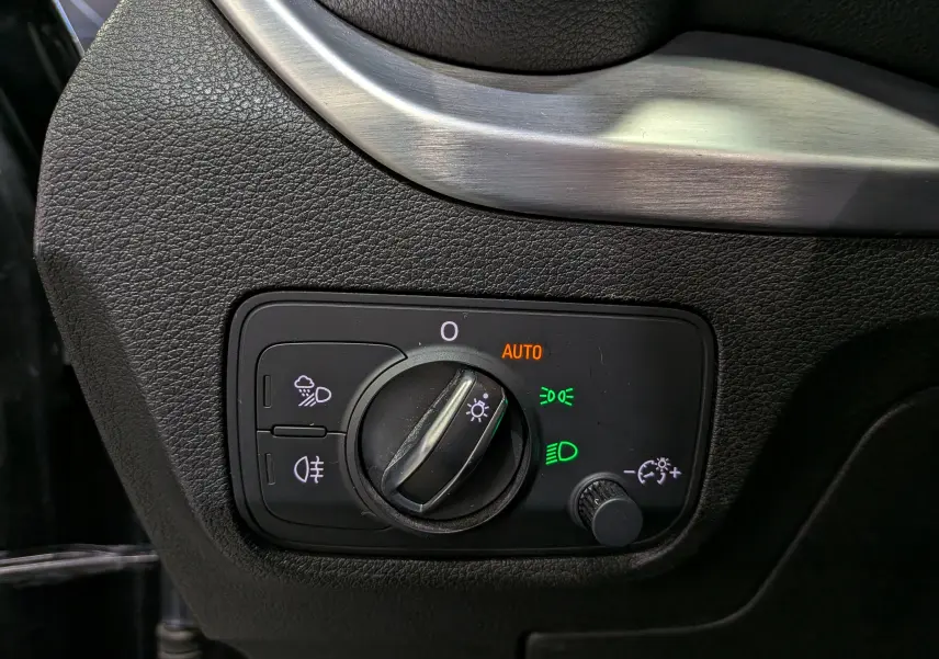 Gros plan sur le bouton de commande des phares avec éclairage automatique sur Audi Q2 gris, intérieur côté gauche.