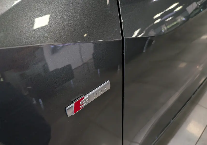 Gros plan sur l'emblème S line sur la portière gris métallisé d'un Audi Q2, soulignant la finition sportive.