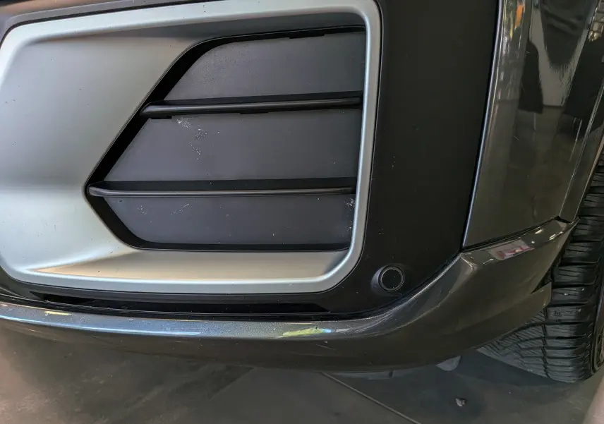 Gros plan sur la partie avant droite grise de l'Audi Q2 1.4 TFSI S-Line, mettant en valeur la grille d'aération et le pare-chocs.