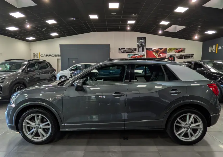 Audi Q2 gris vue de profil côté gauche en intérieur, avec toit contrasté argent et jantes alliage 18 pouces.