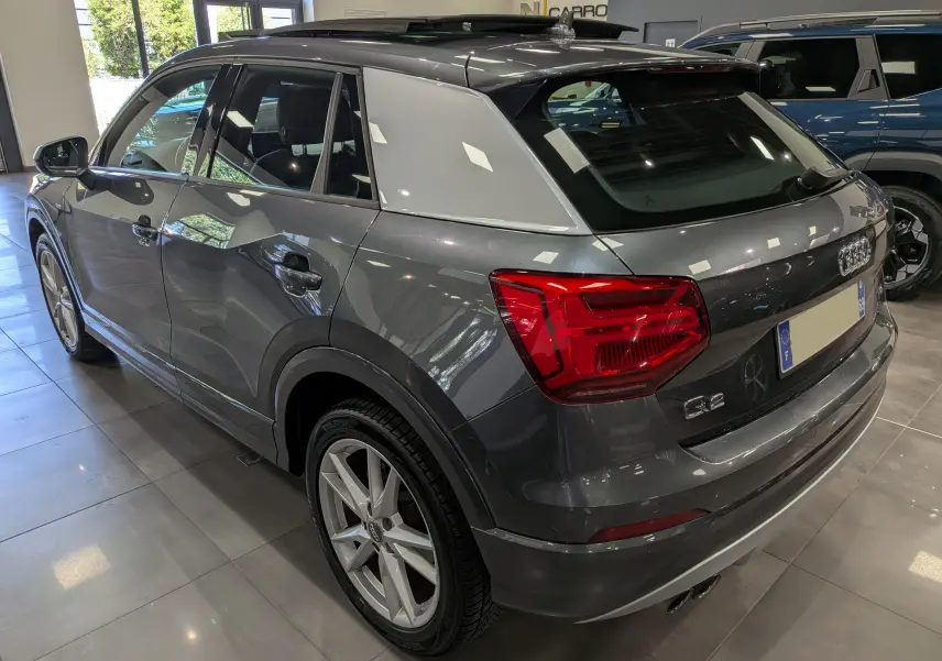 Audi Q2 gris en 3/4 arrière droit, avec jantes alliage et toit noir contrastant, en intérieur showroom.
