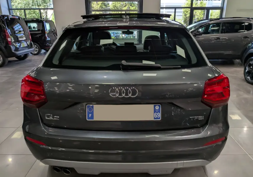 Vue arrière d'un Audi Q2 gris 2017 avec feux rouges et double sortie d'échappement visible en intérieur showroom.