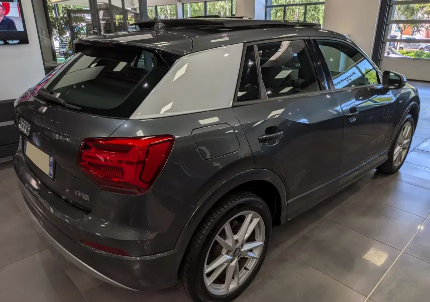 Audi Q2 gris avec toit blanc, vue 3/4 arrière droit, jantes alliage et feux arrière LED en intérieur showroom.