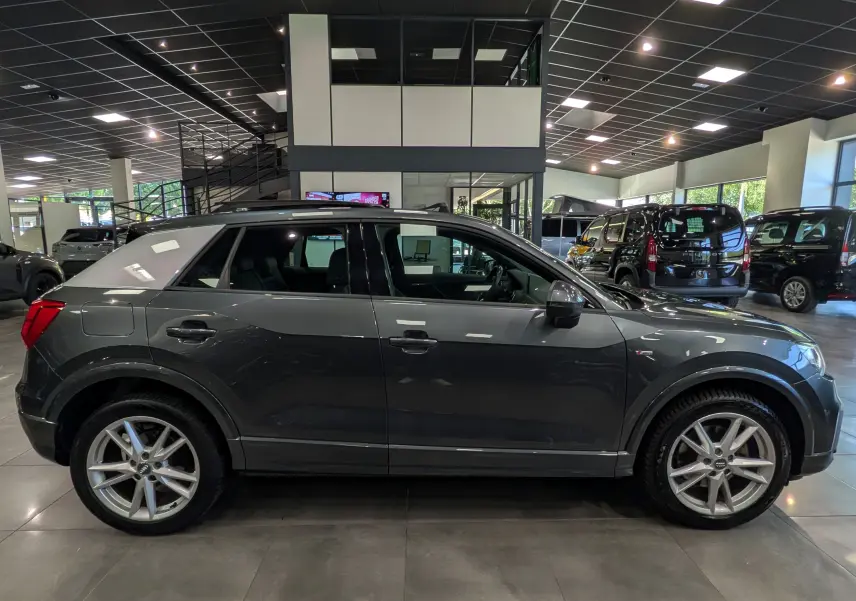 Audi Q2 gris en vue de profil côté gauche, avec toit contrasté blanc et jantes alliage 18 pouces en showroom.