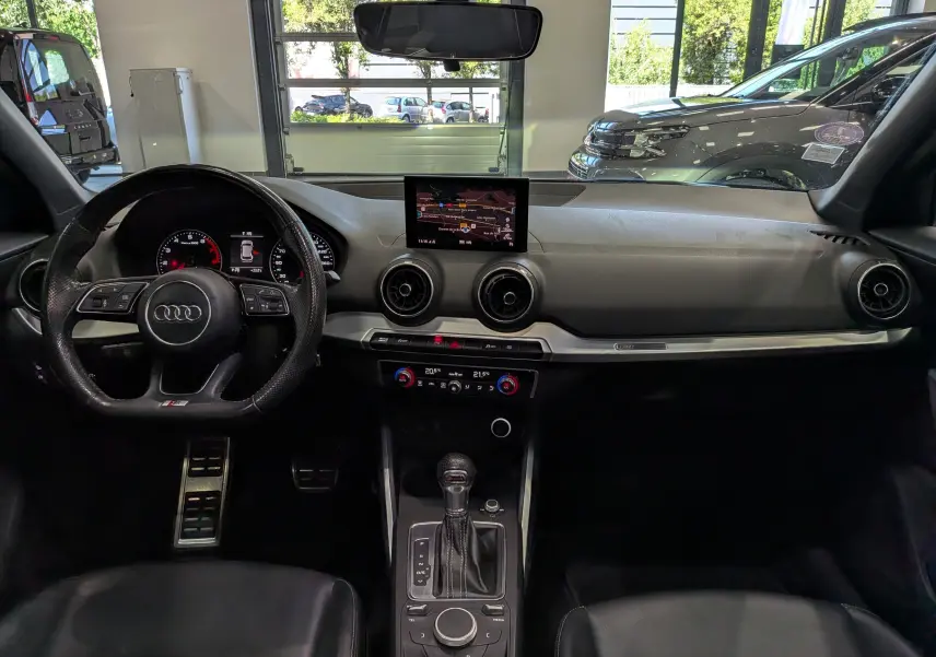 Vue intérieure de l'Audi Q2 1.4 TFSI S-Line 2017, tableau de bord noir avec écran central et volant multifonction.