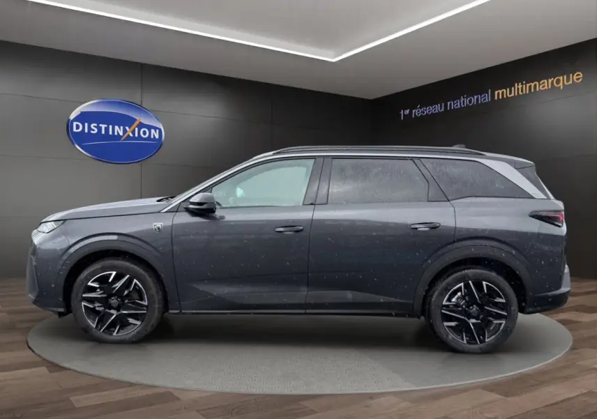 Vue de profil côté gauche d’un Peugeot 5008 gris foncé avec jantes noires et toit noir en showroom.