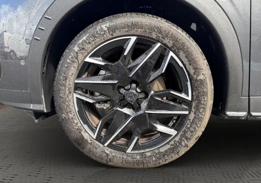 Gros plan sur la roue avant gauche d’un Peugeot 5008 gris foncé avec jante alliage noire et argentée, pneu boueux.