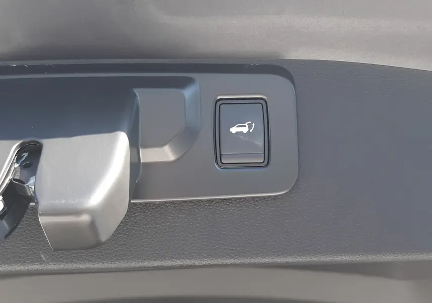 Bouton d'ouverture électrique du hayon sur la partie intérieure du coffre du Renault Symbioz gris cassiopée.
