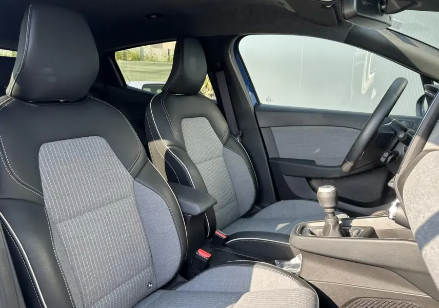 Intérieur avant de la Renault Clio TCE 90 Techno 2025, sièges tissu gris et noir, volant multifonction et levier de vitesse manuel.