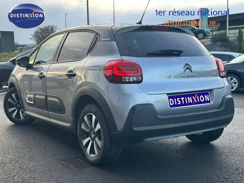 Citroën C3 gris vue 3/4 arrière droit, avec feux arrière distinctifs et protections latérales noires.