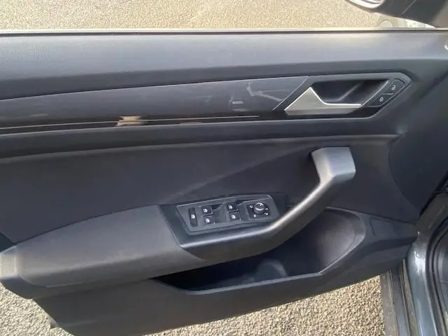 Vue intérieure côté gauche de la porte avant d’un Volkswagen T-Roc gris Indium, avec commandes de vitres et poignée intégrée.