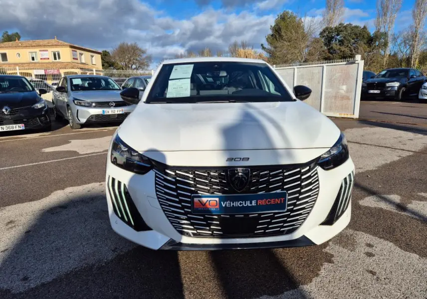 Vue avant d'une Peugeot 208 Hybrid 136 e-DCS6 GT blanche, avec calandre noire et feux diurnes LED verticaux.