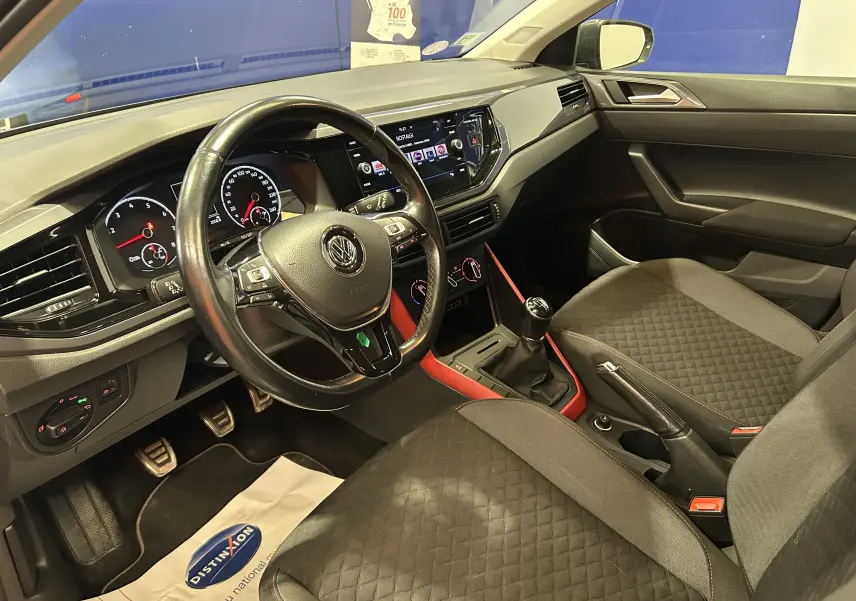 Vue intérieure côté conducteur de la Volkswagen Polo gris 2018, avec volant cuir, console centrale rouge et sièges tissu noir.