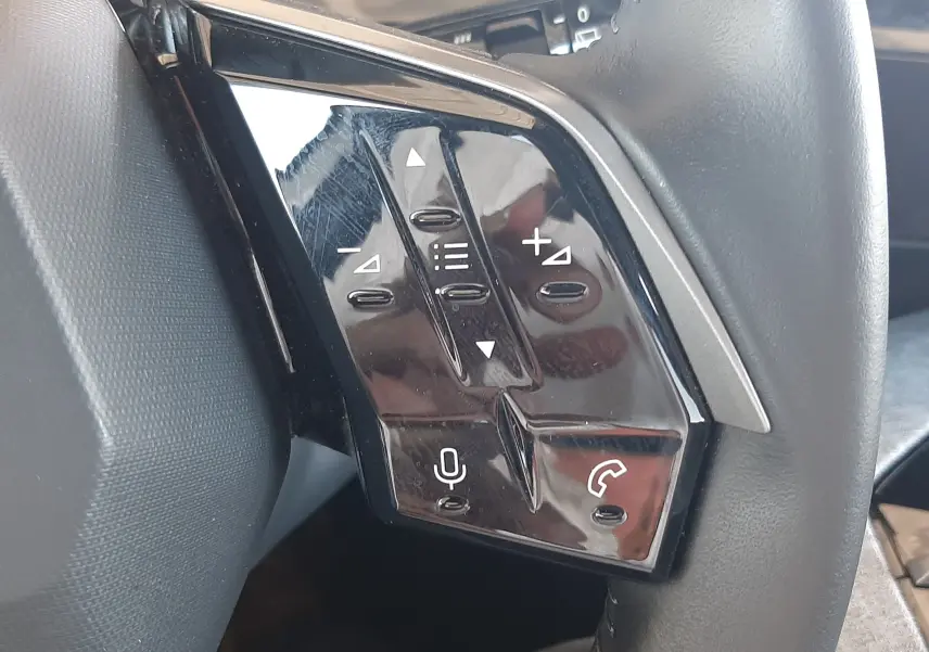 Gros plan sur les commandes multifonctions noires à gauche du volant du Peugeot 5008 Hybrid blanc Okenite 2025.