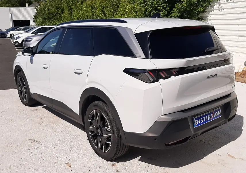 Vue 3/4 arrière droite du Peugeot 5008 blanc Okenite avec jantes noires et vitres teintées, stationné en extérieur.