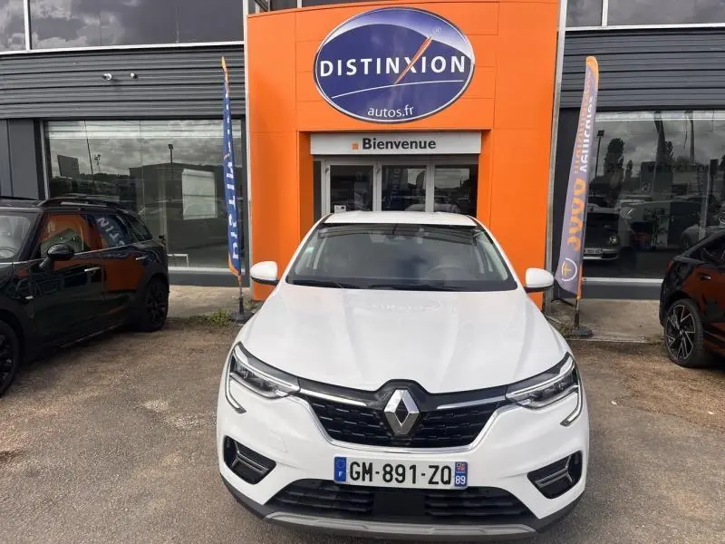 Vue frontale d'un Renault Arkana blanc perle garé devant une concession avec logo Distinxion orange.