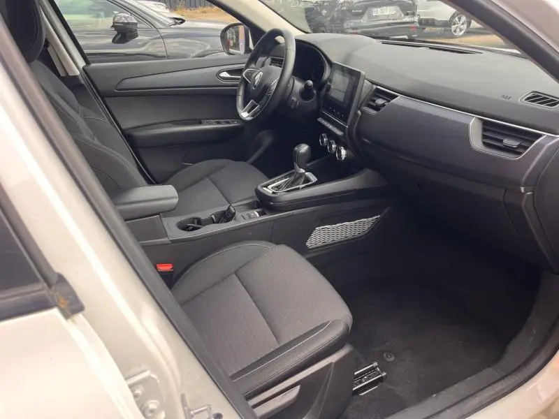 Intérieur avant droit du Renault Arkana blanc perle 2023, sièges noirs, console centrale avec écran tactile et volant cuir.