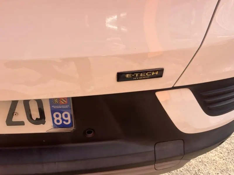 Gros plan sur l'arrière blanc perle d'une Renault Arkana avec badge E-Tech Hybrid et partie du pare-chocs noir.