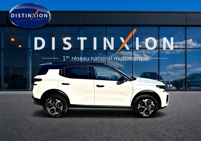 Profil droit d'un Citroën C3 Aircross blanc avec toit noir, jantes alu et vitres teintées devant une vitrine Distinxion.