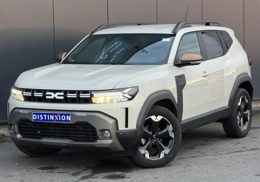 Dacia Duster beige Sandstone en 3/4 avant droit avec jantes alliage noires et barres de toit grises.