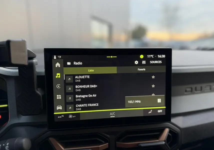 Vue intérieure centrée sur l'écran tactile 10 pouces du Dacia Duster beige Sandstone, avec commandes radio DAB affichées.