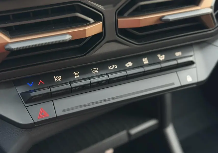 Gros plan sur les commandes de climatisation et les aérateurs avec inserts cuivrés du Dacia Duster Beige Sandstone 2025.