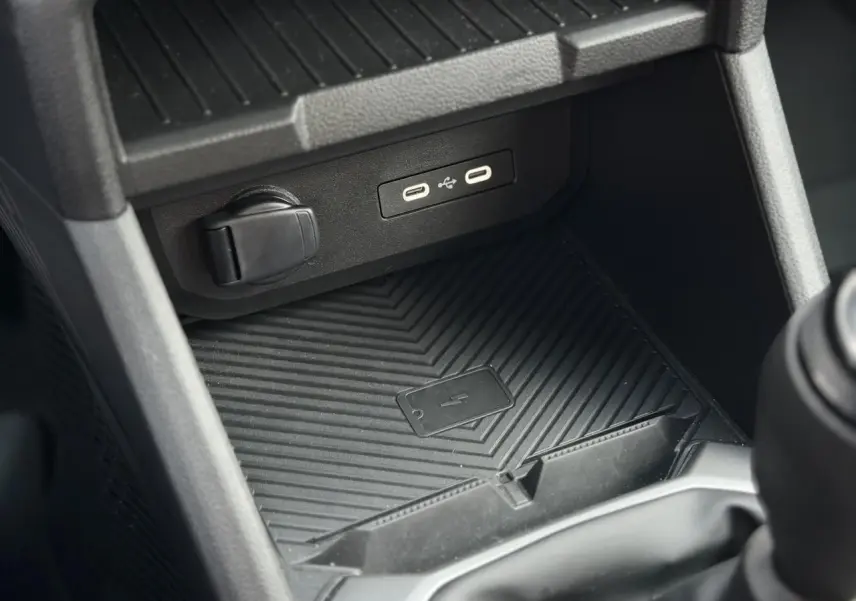 Gros plan sur la console centrale noire du Dacia Duster 2025, montrant la zone de charge à induction avec ports USB.