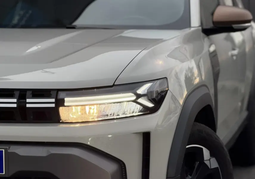 Gros plan sur l'avant droit beige Sandstone du Dacia Duster 2025, mettant en valeur son phare LED et la calandre noire.