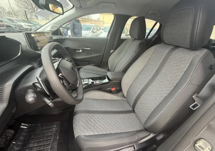 Vue intérieure côté conducteur de la Peugeot 208 gris 2025, montrant sièges tissu et cuir, volant réglable et écran tactile.