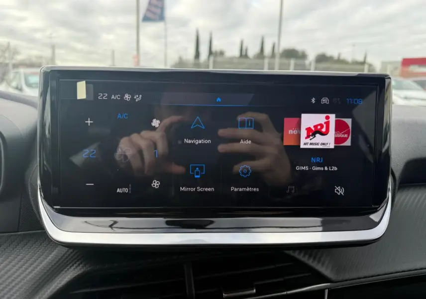 Écran tactile central du tableau de bord de la Peugeot 208 gris, affichant les options de navigation et radio NRJ.