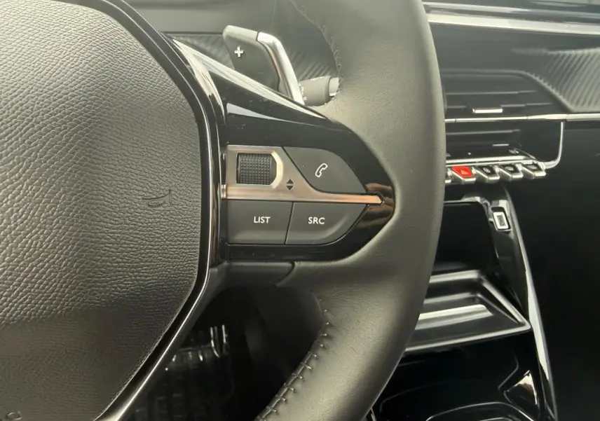 Gros plan sur le volant noir et les commandes multimédia d’une Peugeot 208 Hybrid 145 Allure, intérieur moderne et épuré.