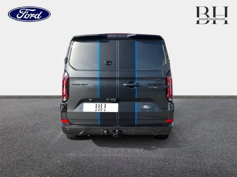Vue arrière d'un Ford Transit Custom gris Magnetic métallisé avec bandes bleues et crochet d'attelage visible.